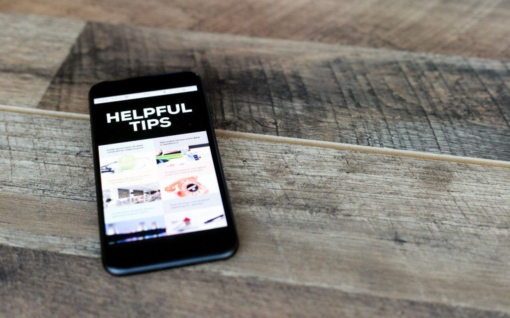 A smartphone on a wooden surface displays a website with the headline "Helpful Tips" and several article previews below it.