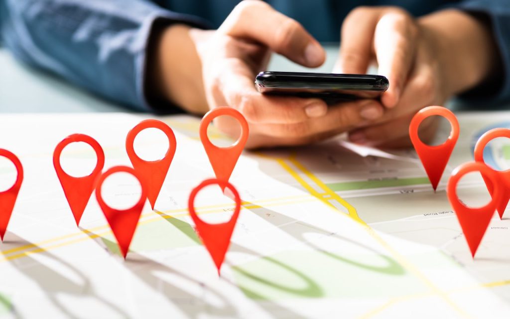 A person using a smartphone above a map with multiple red location markers placed on it.