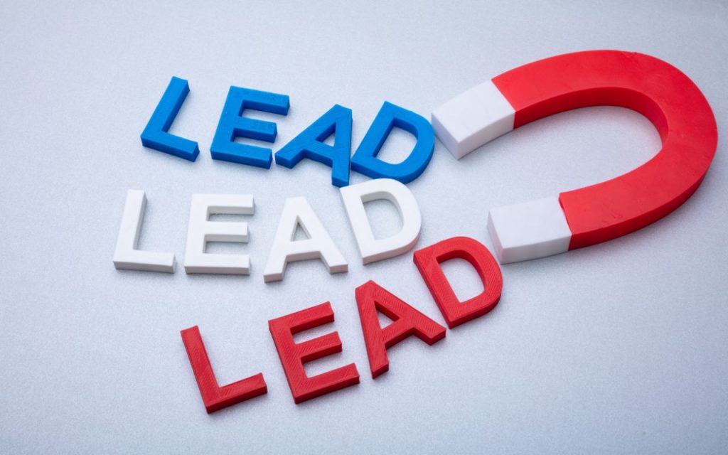 A red horseshoe magnet attracts the word "LEAD" in blue, white, and red letters arranged on a light grey surface.