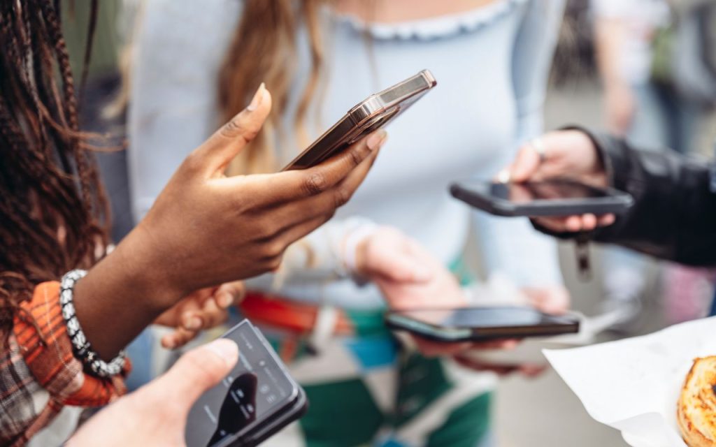Four people are holding and using smartphones, their faces out of frame, with focus on their hands and devices.