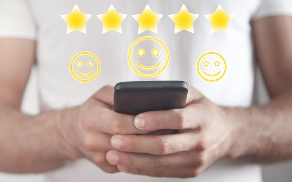 A person holding a smartphone with five yellow stars and three smiley faces floating above the device, suggesting a positive review or high rating.