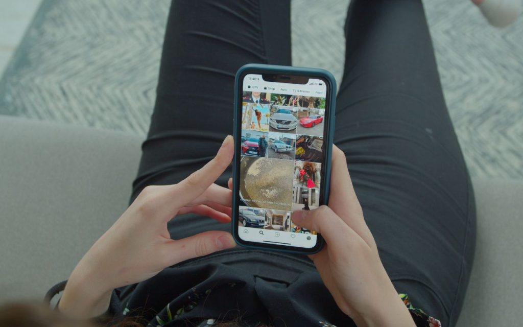 A person holding a smartphone and browsing an image gallery while sitting on a couch with crossed legs.
