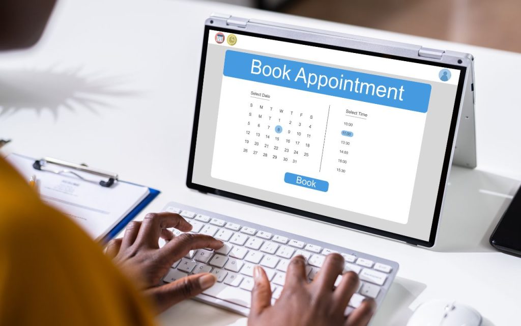 A person is using a keyboard to book an appointment online on a tablet, which displays a calendar and time selection screen.