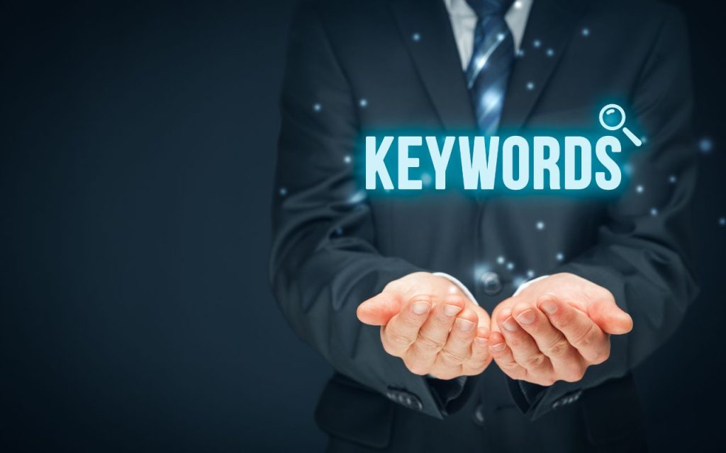 A person in a suit holds out cupped hands with the word "KEYWORDS" and a magnifying glass icon digitally displayed above them.
