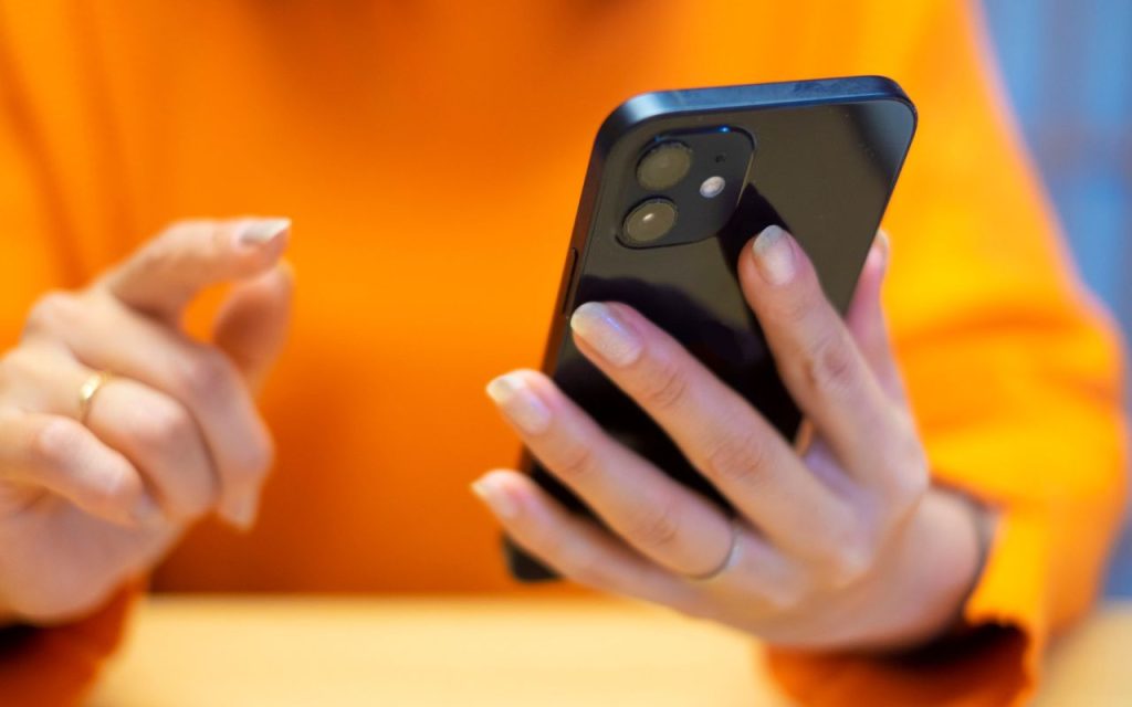 A person wearing an orange shirt holds a black smartphone in one hand and is about to tap the screen with the other hand to view TikTok's Local Feed feature.